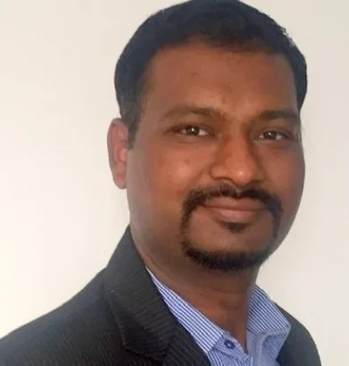Portrait of a man with short dark hair and a goatee, wearing a dark blazer and blue striped shirt, looking at the camera.