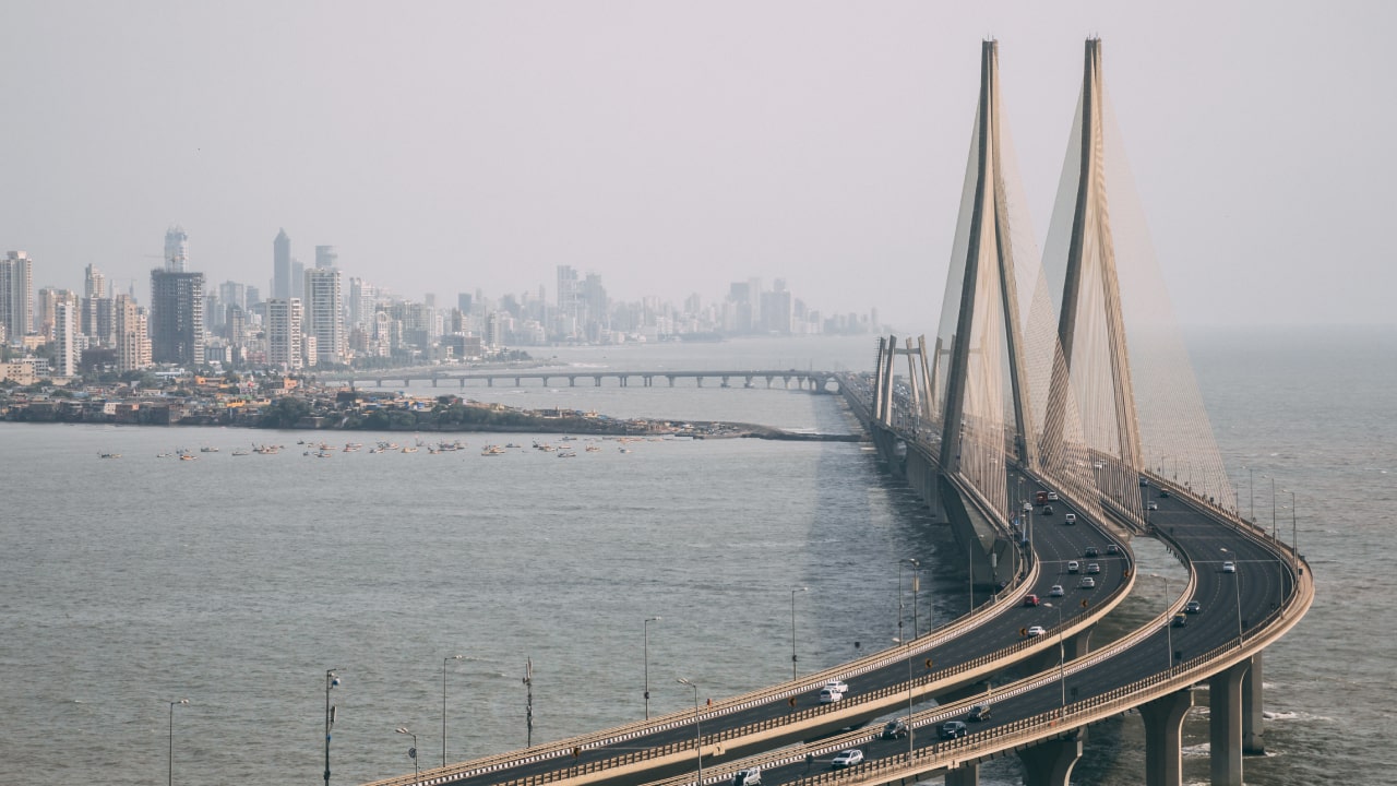 A modern bridge spans over water, connecting urban areas with skyscrapers in the background and boats on the water.