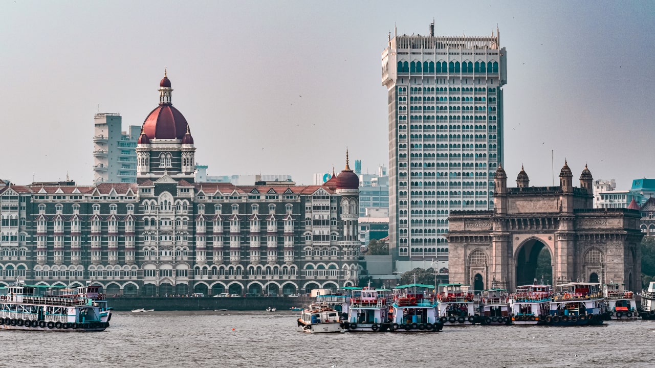 A scenic view of Mumbai featuring the Taj Mahal Palace hotel, Gateway of India, and boats on the water.